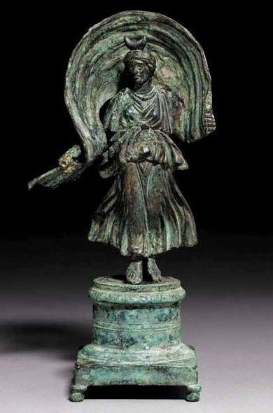 Bronze figurine of Diana-Selene. The goddess wears a crescent-moon ornament in her hair. The statue has been identified with Selene, due to the presence of the crescent moon on her head and the torch in her right hand, attributes characteristic of the goddess.
The goddess (personification of the Moon) is wearing a sleeveless, high-girded peplos, which gathers on her breasts and legs revealing her figure, and then gathers at the hem and in the folds that fall alongside her, pushed by the impetus…