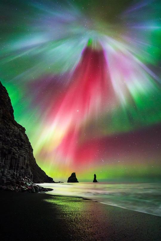 Intense red & green aurora over a beach.
