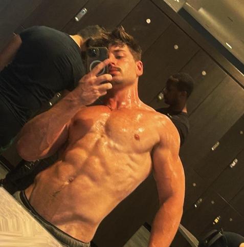 A sweaty muscular man is taking a selfie in a locker room showing his sweaty chest