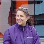 Foto van een lachende Bianca, lang donker haar in een paardenstaart en met paars piratenpartij-regenjasje aan.