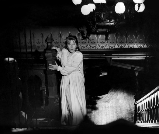 an image of a woman in a white sleeping dress holding onto a banister, looking at the staircase