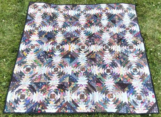 a quilt, it is a dense pattern, there are many rows and in the windows of the rows are designs done in floral fabrics, a square center with angular columns radiating out in the 4 directions 