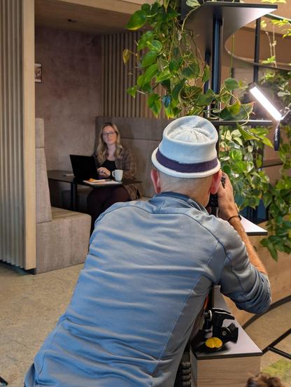 Ein Fotograf macht ein Bild von einer Mitarbeiterin die an einem Tisch sitzt