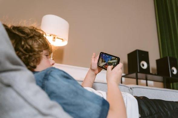 Ein Junge liegt auf dem Sofa und spielt ein Spiel auf dem Smartphone