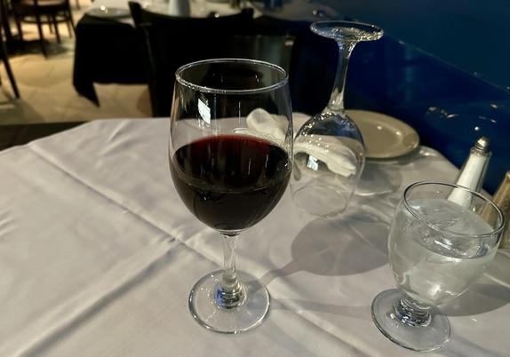 Weiss gedeckter Tisch, ein sehr grosses, sehr gut gefülltes Glas Rotwein steht darauf.