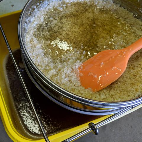 The stainless sieve with an orange silicone spatula sitting on top of the bucket with honey in it. The sieve is full of wax capping that plug the screen when the honey level drops so the spatula lifts it back up and it starts flowing again until the lower finer screen plugs up but that's at the end so the upper screen can be taken off and then the lower one scraped to allow the last honey to drain through.
