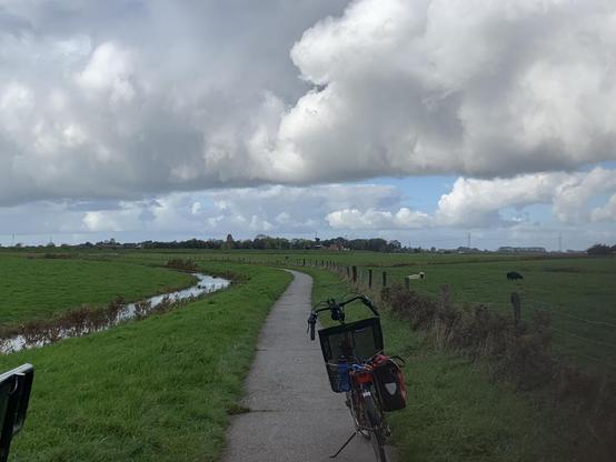 Fietspad met ligfiets en sloot ernaast en bovenal veel wolken met wat blauw ertussen.