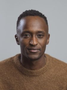 Foto van Jean-Aimé, glimlach, kort donker haar, bruine trui.