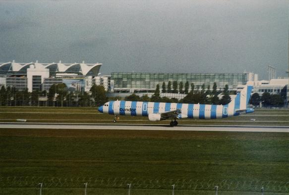 Viewed from the side, a vertically striped plane lands at an airport runway with its front wheel still in the air.