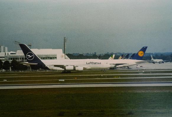 Viewed from the side, multiple planes stand behind each other at an airport.