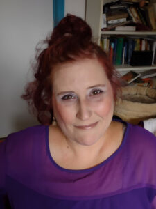 Foto van een gimlachende Sabrina, donkerrode haren en een paars shirt. 