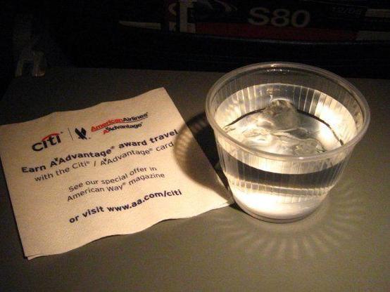 photograph of an airline seat tray with a clear plastic cup of ice water and a napkin. Photo attribution: Flickr user ineffablepulchritude