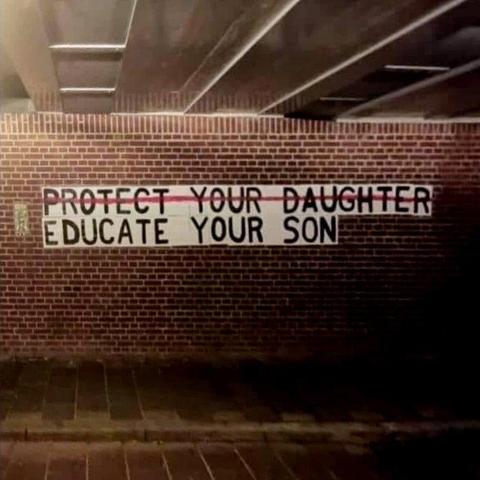 Auf einer Klinker-Mauer steht geschrieben:

PROTECT YOUR DAUGHTER (mit rot durchgestrichen)
EDUCATE YOUR SON