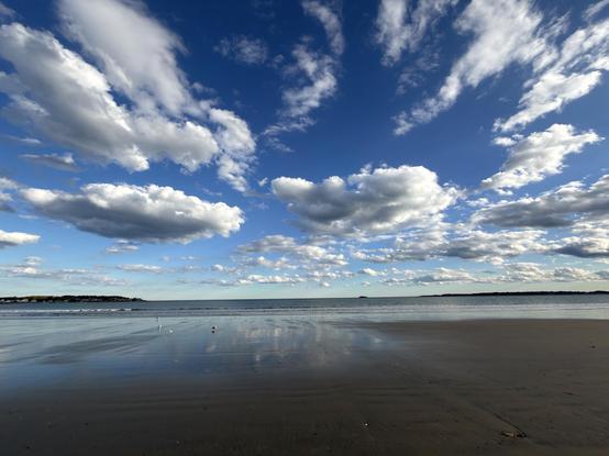 A beach with flowing water, gritty sand and a blue cloud strewn sky.