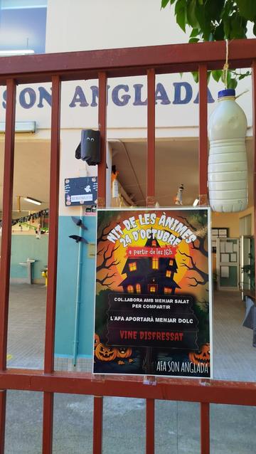 Vista del cartell de la festa sobre la tanca. A darrera s'hi veuen diverses decoracions per ambientar-la. A dalra es llegeix "Son Anglada" sobre la façana de l'escola.
