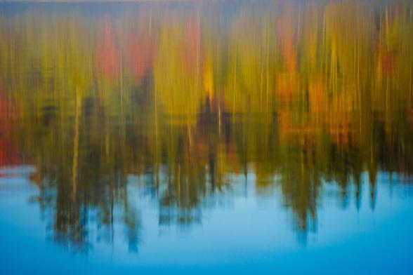 A blurred reflection of colorful trees in calm water, showcasing fall colors.