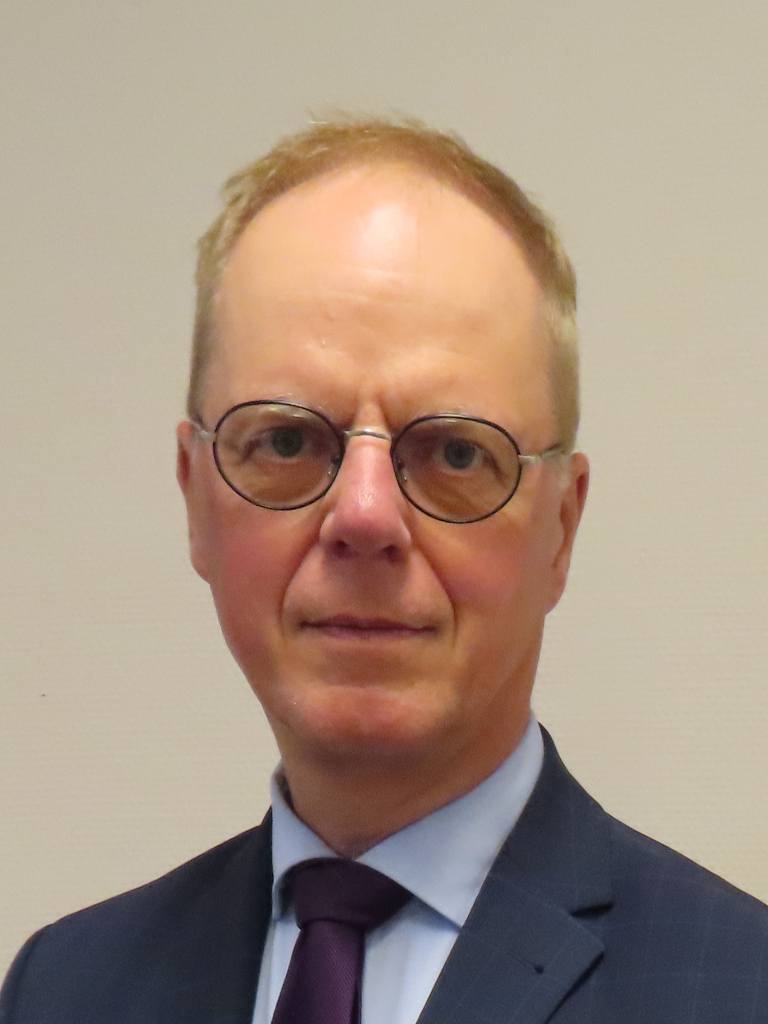 Foto van Wietze, kort, blond haar, bril. Blauw jasje, met paarse piratenstropdas en lichtblauw overhemd. 