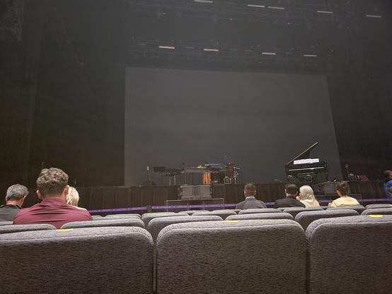 Interior photo from our seats in Section 1 Row F. On the stage is a dimly-lit group of musical instruments, the main focus is a Steinway piano.