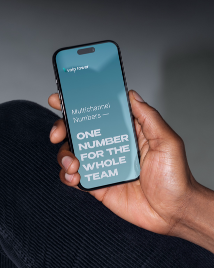 A person holding a smartphone displaying a VoipTower screen with the text “Multichannel Numbers — One number for the whole team,” representing VoIP telephony and unified business communication.