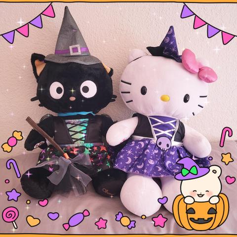 Build a Bear Chococat and Hello Kitty are wearing witch outfits. Chococat has a black dress with red and green stars, and a grey and purple witch hat, and is holding a broom. Hello Kitty is wearing a purple witch dress with skulls and moons, and a small purple witch hat.