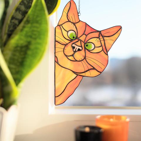 An orange stain glass cat peeking into a window right at you!