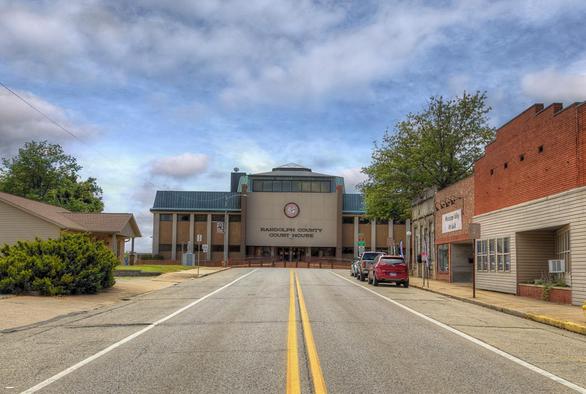 A courthouse stands prominently at the end of a small-town street, flanked by a red brick building and other structures.