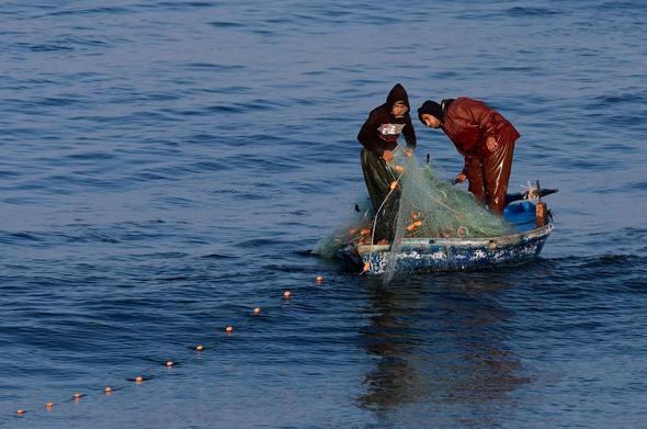Two fisherman in a small boat with a net.