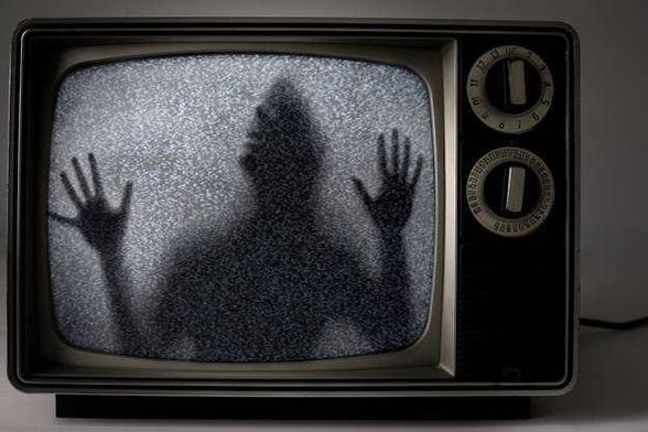 A 1980s woodgrain TV. Approximately 13 inches, and has analog dials on the front. There is a shadow of a human screaming like they’re trapped within the TV screen. 