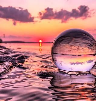 A beautiful artwork of gorgeous multi colorful water with a clear crystal ball floating in the water and reflecting the sky and water and it's a very pretty scene.