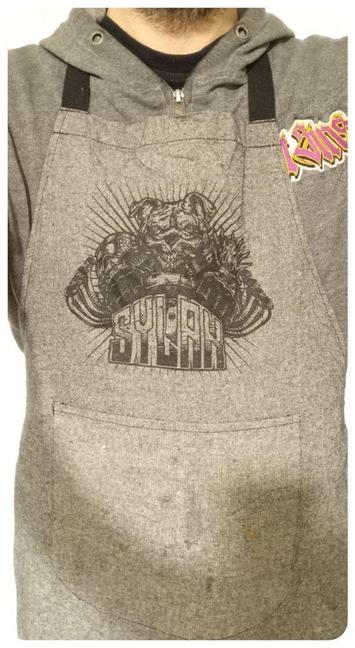 Magnifique tablier du Sylak, acheté cette année. 
Tout gris avec une impression noire. 
Le dessin reprend le bouledogue en version Mad Max avec respirateur et tuyauterie. 
Pas le plus joli mais comme c'est en noir sur gris, ça ne se voit pas trop...