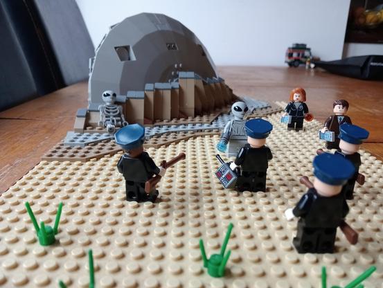 Some LEGO cops facing a UFO survivor with rifles, Mulder and Scully standing by to negotiate, crashed UFO in the background