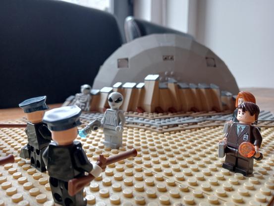 Some LEGO cops facing a UFO survivor with rifles, Mulder and Scully standing by to negotiate, crashed UFO in the background