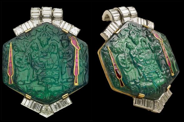 Broche de plata con una esmeralda hexagonal con un relieve de una persona con un niño en la falda. A sus lados hay otras dos personas de pie.