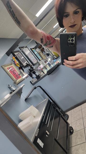 Sheryl shows her new bicep tattoo, that reads "Fund Abortion, Not War" around a feminism triangle filled with red and green flowers and a keffiyeh pattern. 