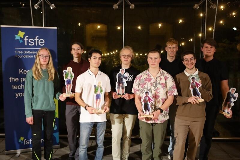 8 young people with awards in front of a banner.