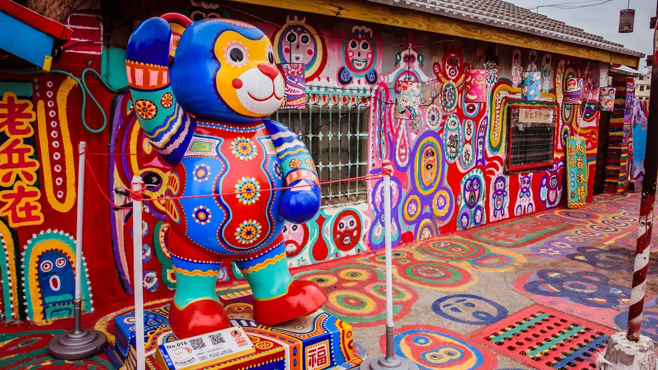 Das Bild zeigt das berühmte „Regenbogendorf“ (Rainbow Village) in Taichung, Taiwan.
Es ist ein bunt bemaltes Viertel, das ursprünglich aus alten Militärunterkünften bestand. Ein pensionierter Soldat namens Huang Yung-Fu, heute bekannt als „Grandpa Rainbow“, begann in den 2000er-Jahren, die Häuser mit leuchtenden Farben, Mustern und Figuren zu bemalen, um sie vor dem Abriss zu retten.
Heute ist das Dorf eine der beliebtesten Touristenattraktionen Taichungs.
Die farbenfrohen Wände, Böden und Skulpturen – wie die große bunte Bärenfigur im Vordergrund – sind typisch für den verspielten und einzigartigen Stil des Künstlers.
Kurz gesagt:
Ein Ort voller Farben, Symbolik und Lebensfreude – entstanden aus einer Rettungsaktion, die zu einem kulturellen Wahrzeichen wurde.