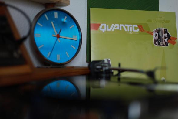 We see the cover of Quantic - The 5th Exotic Vinyl Album behind a blurred turntable. 
