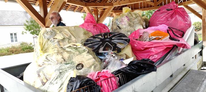 des sacs de déchets jaune et roses, entassés sur une remorque, sous une halle.
