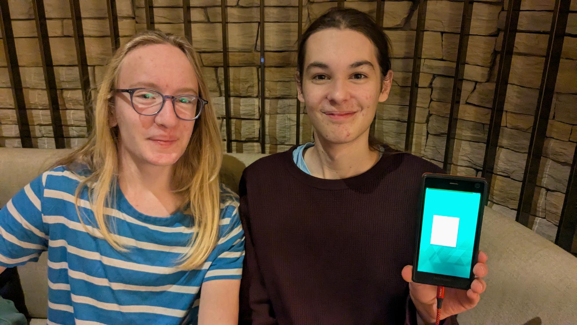 two people one of them holding a phone running a window manager.