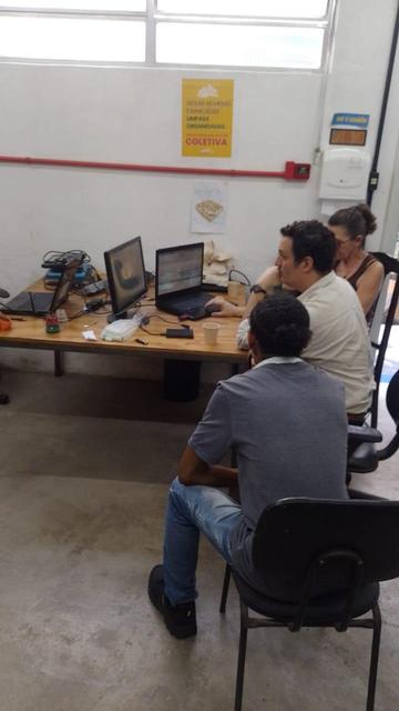 3 pessoas ao redor de uma mesa olhando a tela de um computador instalando Linux