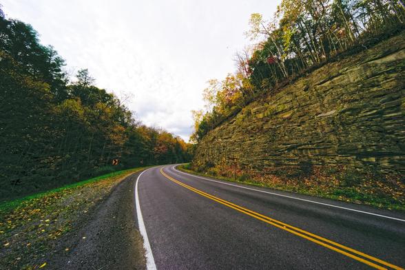 road starts from the lower right and heads diagonally towards the center before curving back to the right past an outcropping of rock covered with trees