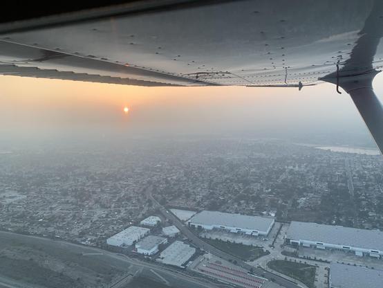 The sun shines through thick haze over a suburban area near sunset, seen from the air