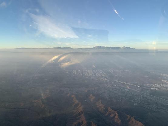 A layer of haze over a suburban area obscure all but the tops of a mountain range beyond