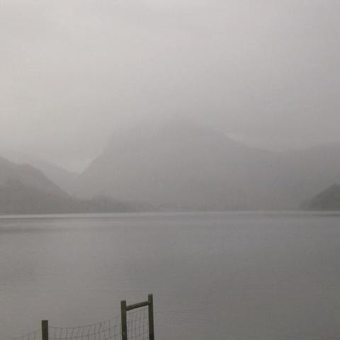 The cover for Damian Scholl's, "On Paths Forgotten" single. It shows a misty lake with a faint mountain backdrop. A wooden post and wire fence in the foreground. Atmosphere is serene and muted in grey.