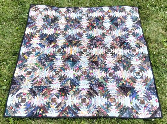 a quilt, it is a dense pattern, there are many rows and in the windows of the rows are designs done in floral fabrics, a square center with angular columns radiating out in the 4 directions