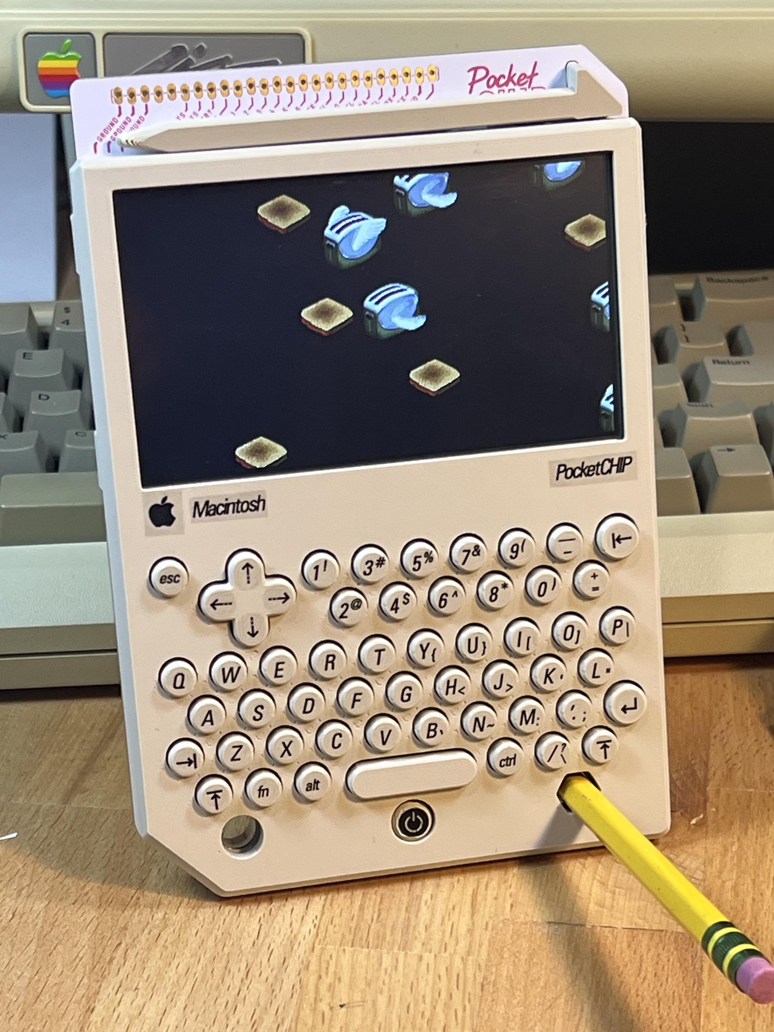 A PocketCHIP hand held computer on a desk using a #2 pencil as a stand. The case is in a warm beige color with round keys. On the screen is the Flying Toasters screen saver from After Dark.