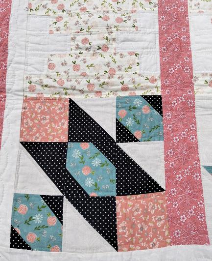 a close-up of one of the regions of the quilt, shapes done with black, blue, and white fabrics with floral printing on them 