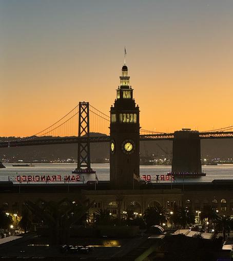 View East from the financial District of San Francisco at sunrise. The ferry building is in the foreground, the bay and Bay Bridge in the background