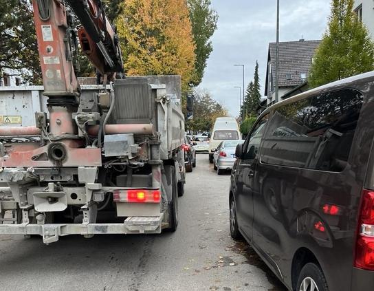 Bild einer Fahrbahn mit rechts parkenden Autos, davon 2 Kleinbusse. Links davon halten mehrere PKW und ein LKW verkehrsbedingt.