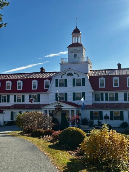 Der mittlere Teil des Hotel Tadoussac. Es zeigt den Turm, der ein wenig an einen Leuchtturm gemahnt. Die Grundfarbe ist weiss, grüne Fensterläden. Der obere Stock und das Dachsind in einem roten Ton gehalten. Die Sonne scheint vom fast makellos blauen Himmel.